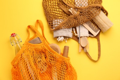 Fishnet bags with different items on yellow background, flat lay. Conscious consumption