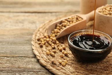 Photo of Pouring soy sauce into bowl at wooden table, closeup. Space for text