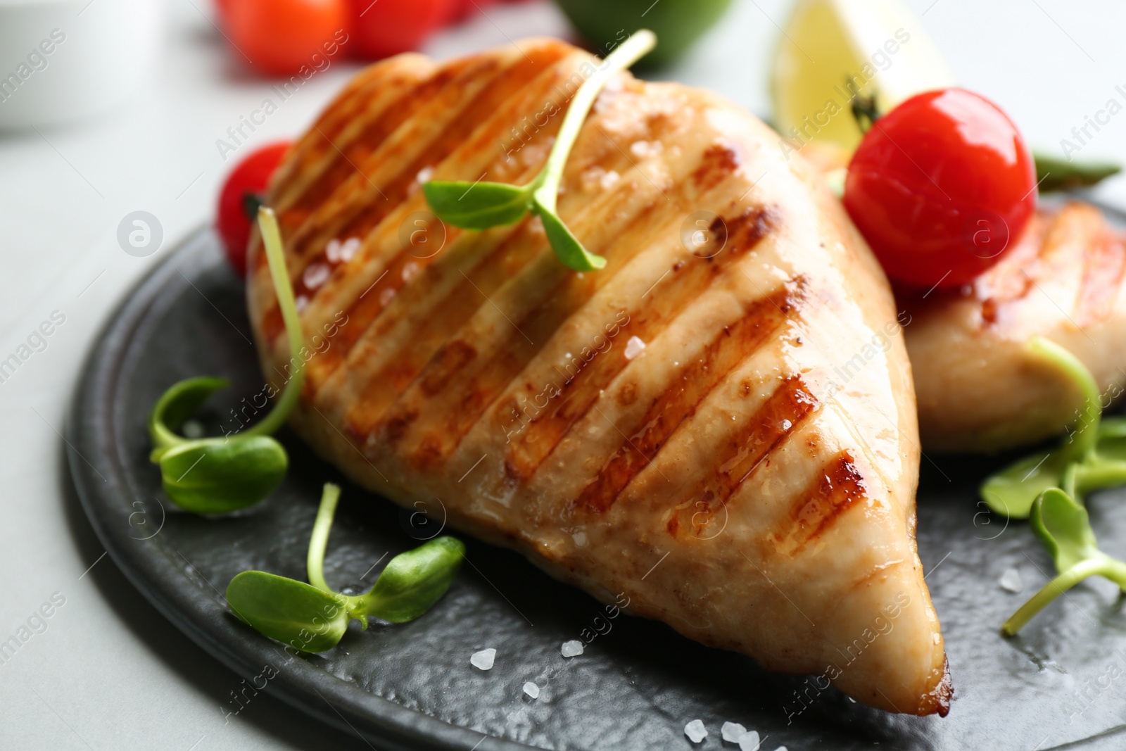 Photo of Tasty grilled chicken fillet with green sprouts on slate board, closeup