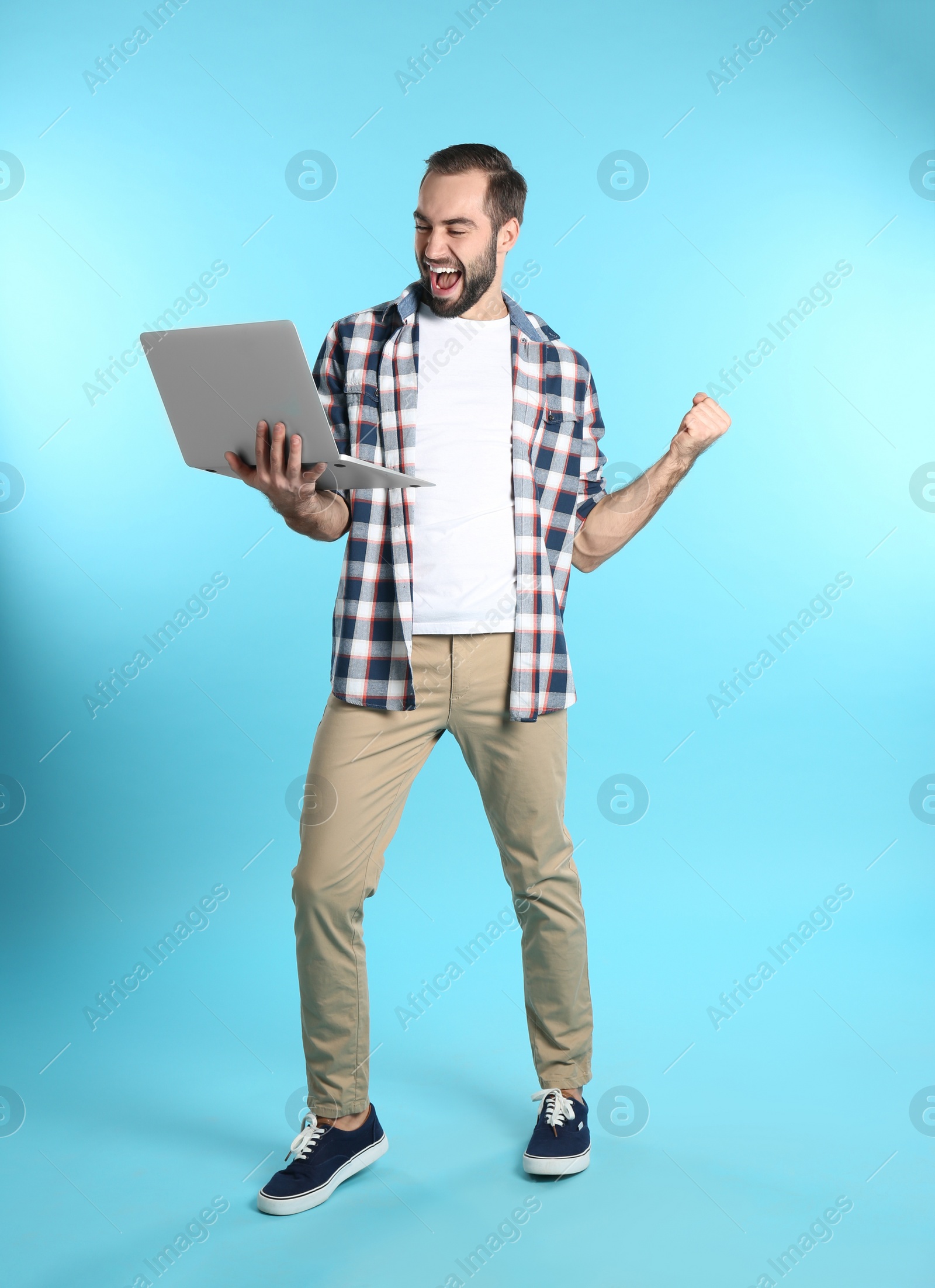 Photo of Emotional young man with laptop celebrating victory on color background