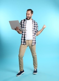 Emotional young man with laptop celebrating victory on color background