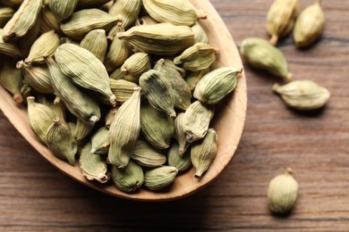 Spoon with dry cardamom pods on wooden table, closeup