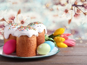 Delicious Easter cakes, tulips and dyed eggs on wooden table outdoors