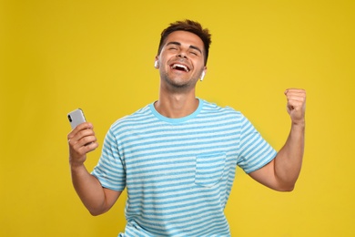 Photo of Happy young man with smartphone listening to music through wireless earphones on yellow background