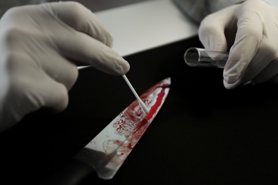 Photo of Detective taking DNA sample of blood from knife at table, closeup