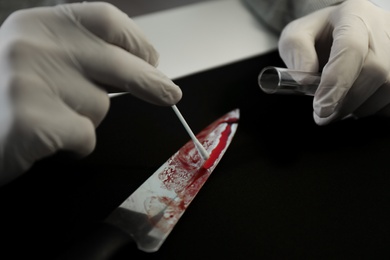 Detective taking DNA sample of blood from knife at table, closeup