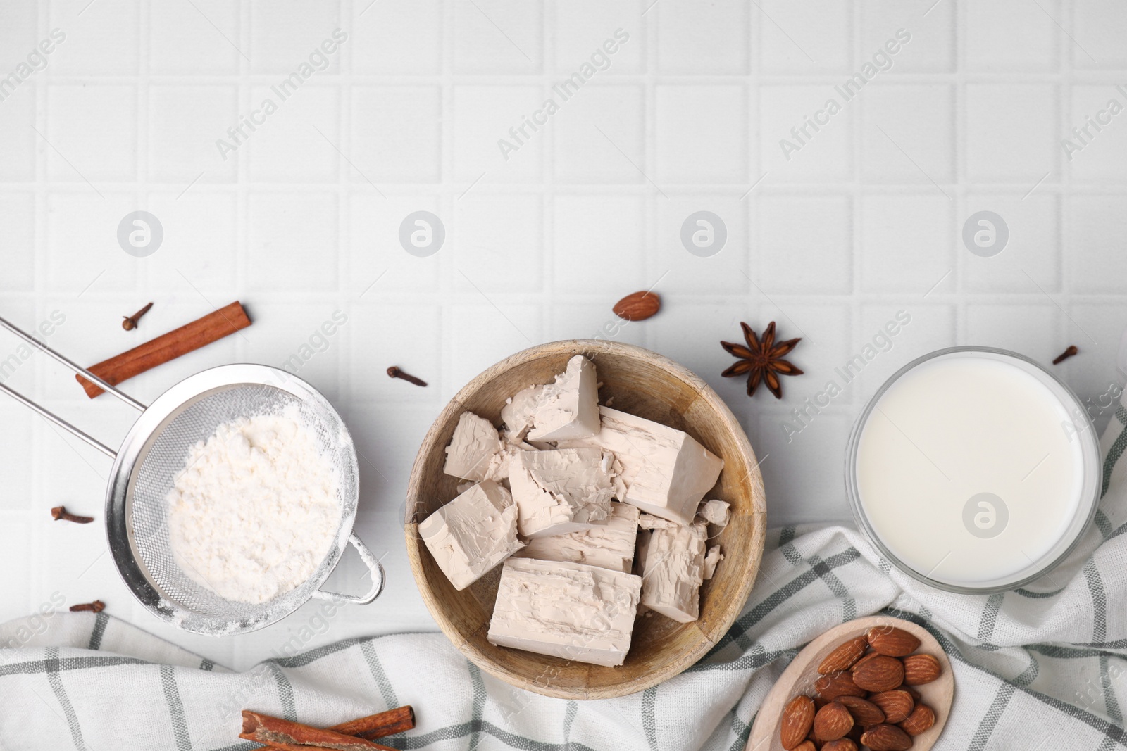 Photo of Bowl with compressed yeast, flour and other ingredients on white tiled table, flat lay. Space for text