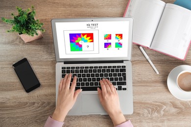 Image of Woman using laptop for taking IQ test at wooden table, top view