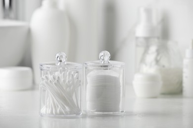 Containers with cotton swabs and pads on white countertop in bathroom