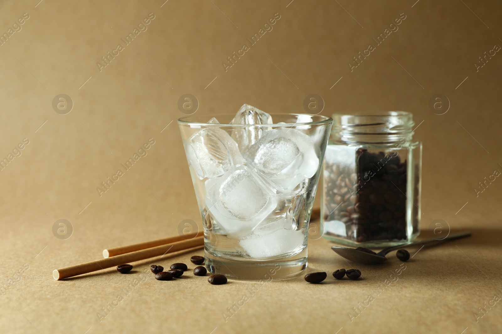 Photo of Cooking iced coffee. Ice cubes in glass, beans and straws on beige background, closeup