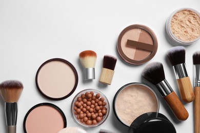 Different face powders and makeup brushes on light background, flat lay