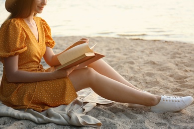 Photo of Young woman reading book on sandy beach near sea, closeup