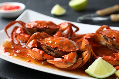 Photo of Delicious boiled crabs with sauce and lime on black table, closeup