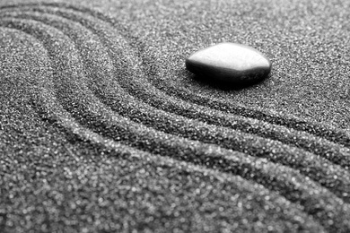 Photo of Zen garden stone on black sand with pattern, closeup
