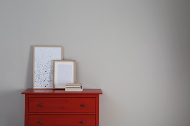 Photo of Red chest of drawers with photo frame, picture and books near light wall, space for text. Interior design