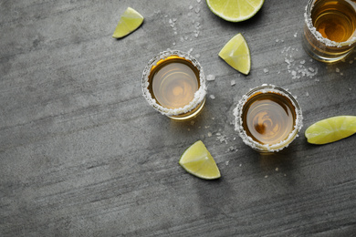 Photo of Mexican Tequila shots, lime slices and salt on grey table, flat lay