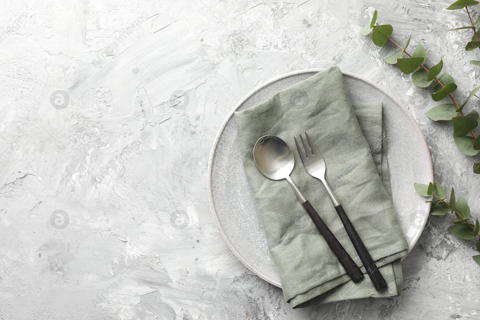 Photo of Stylish setting with cutlery, napkin, eucalyptus branches and plate on grey textured table, flat lay. Space for text