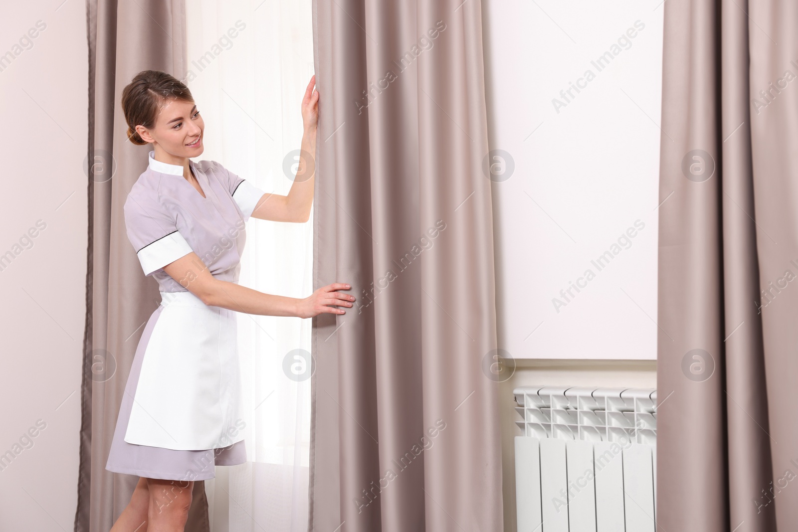 Photo of Beautiful chambermaid opening window curtains in hotel room