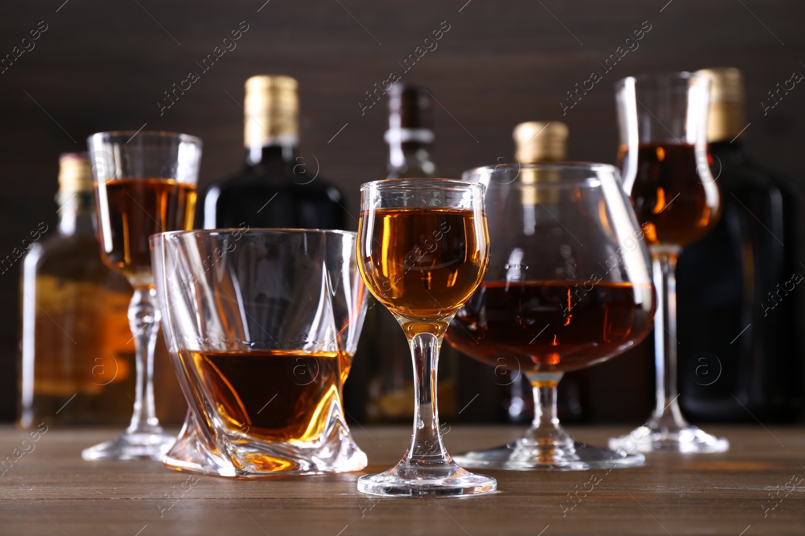 Photo of Different delicious liqueurs in glasses and bottles on wooden table