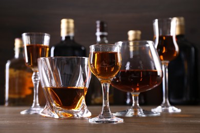 Photo of Different delicious liqueurs in glasses and bottles on wooden table