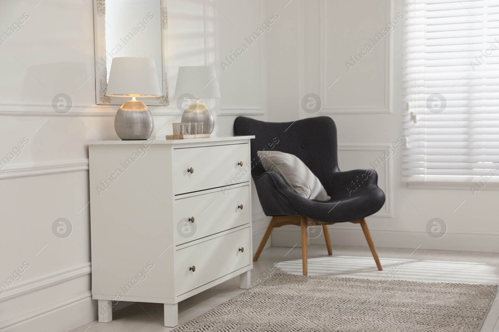 Photo of White chest of drawers, armchair and mirror in room. Interior design