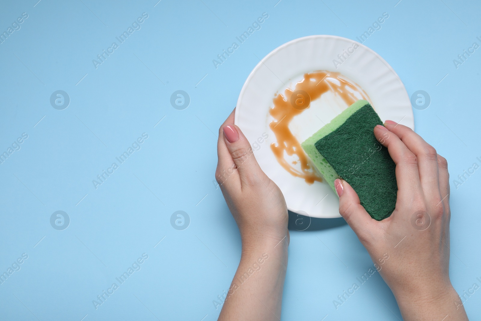 Photo of Woman washing dirty plate with sponge on light blue background, top view. Space for text