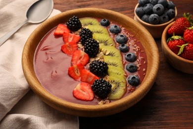 Bowl of delicious smoothie with fresh blueberries, strawberries, kiwi slices and blackberries on wooden table, closeup