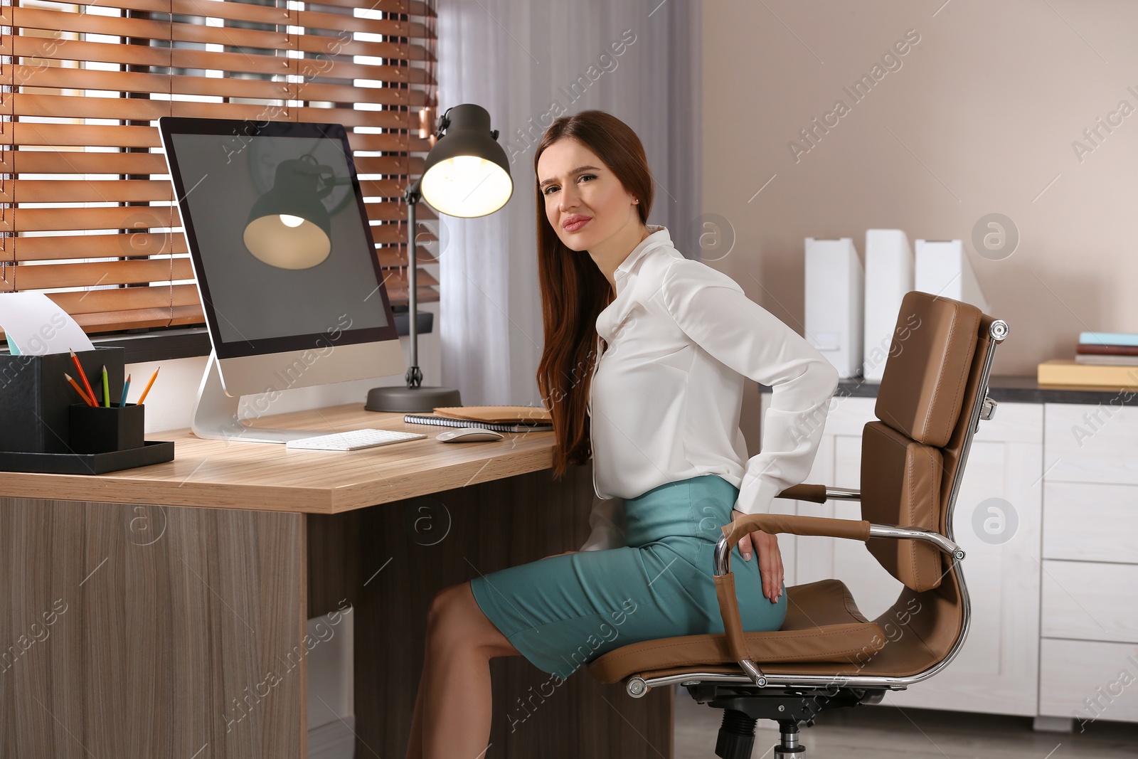 Photo of Young woman suffering from hemorrhoid at workplace in office