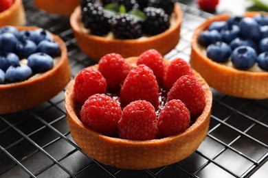 Photo of Tartlet with fresh raspberries on cooling rack, closeup. Delicious dessert