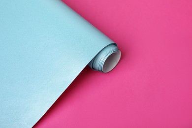 Photo of Roll of light blue wrapping paper on pink background, closeup. Space for text