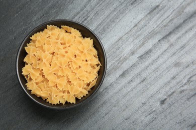 Raw farfalle pasta in bowl on grey table, top view. Space for text