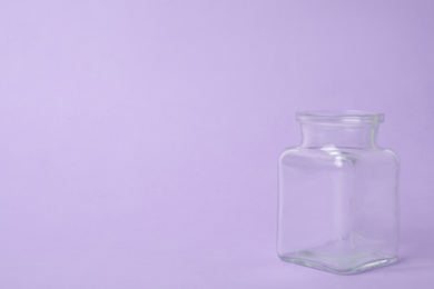 Open empty glass jar on lilac background, space for text