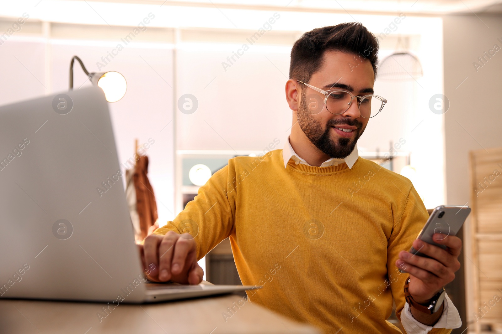 Photo of Man using smartphone while working with laptop in cafe