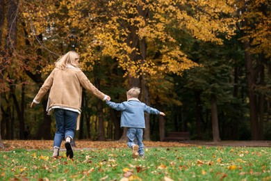 Photo of Mother running with her son in autumn park, back view. Space for text