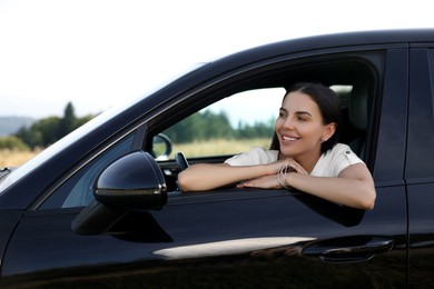 Photo of Enjoying trip. Portrait of beautiful happy woman in car, view from outside