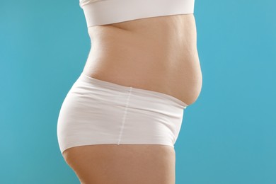 Woman with excessive belly fat on light blue background, closeup. Overweight problem