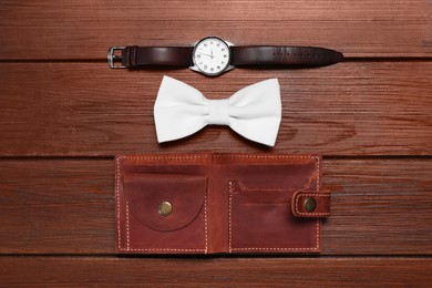 Stylish white bow tie, wristwatch and wallet on wooden background, flat lay