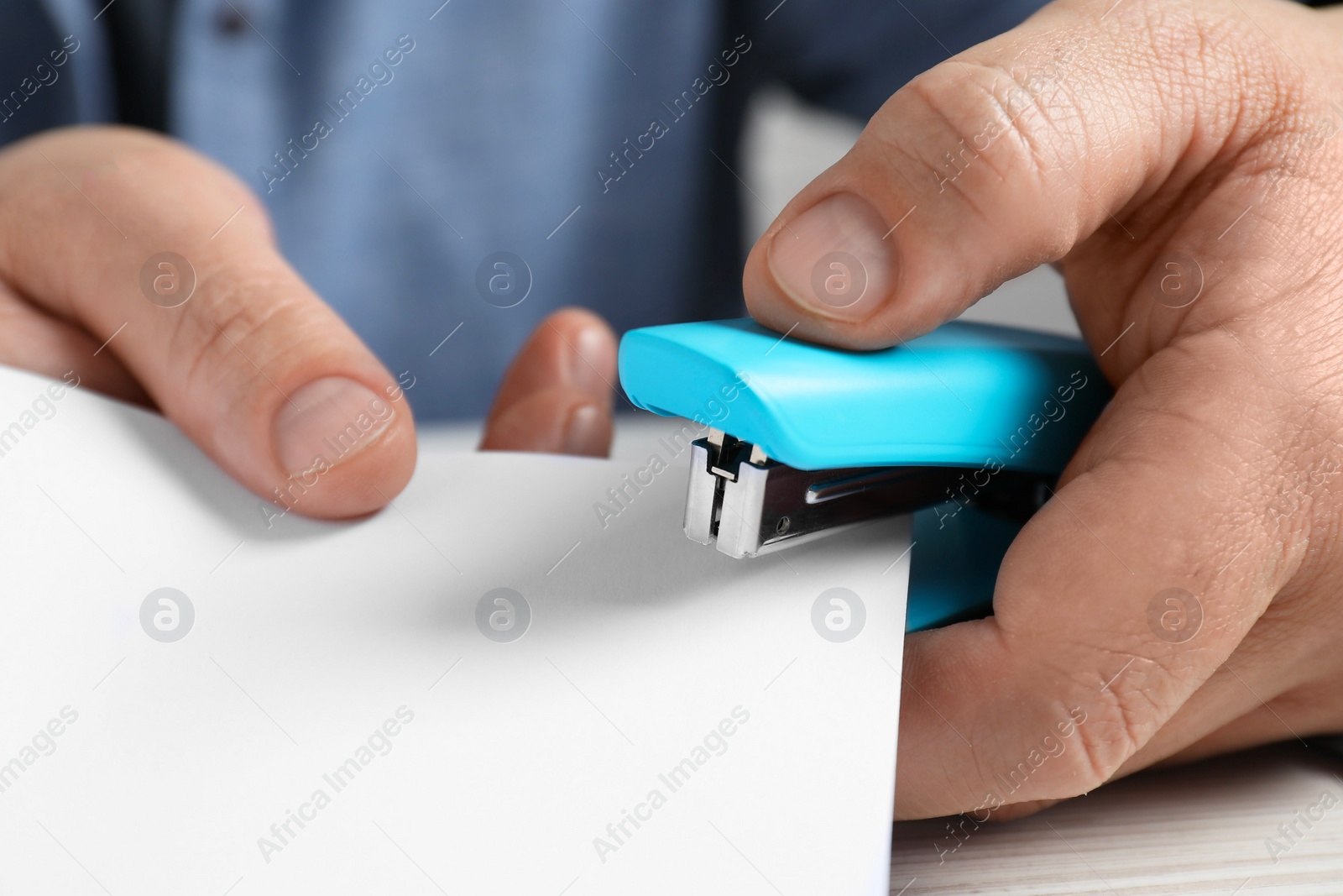 Photo of Man with papers using stapler at white table, closeup