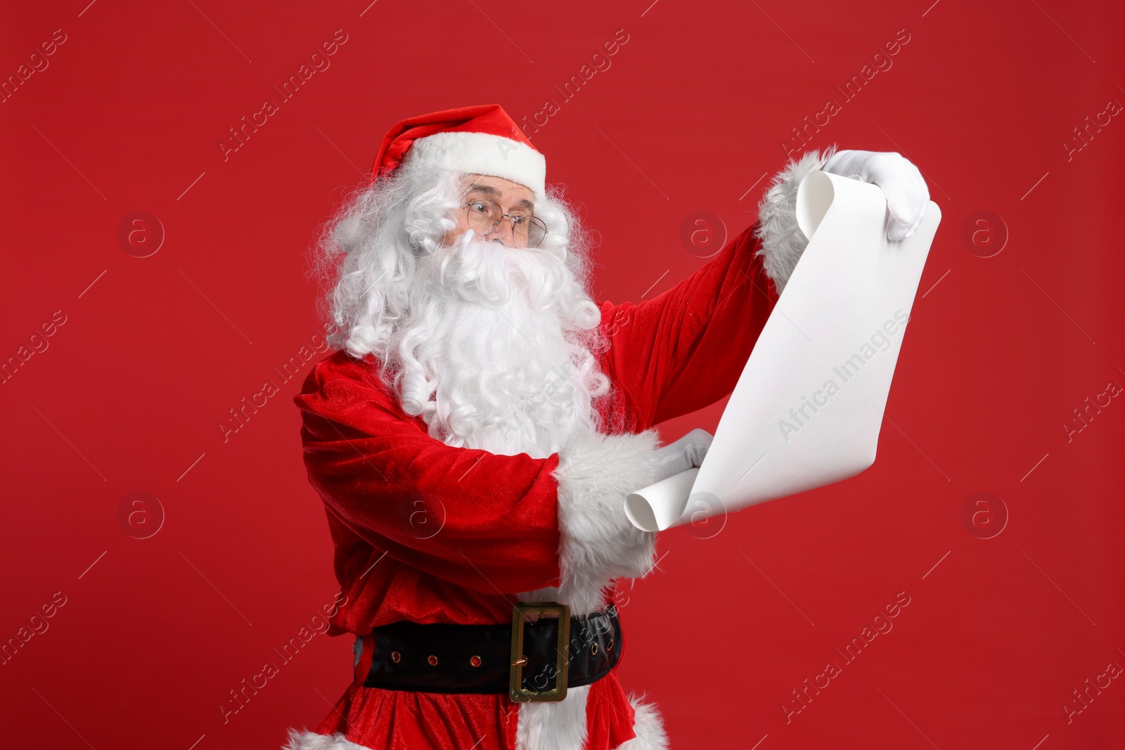 Photo of Merry Christmas. Santa Claus reading wishlist on red background