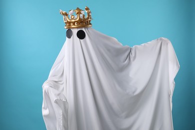 Person in ghost costume and luxurious crown on light blue background