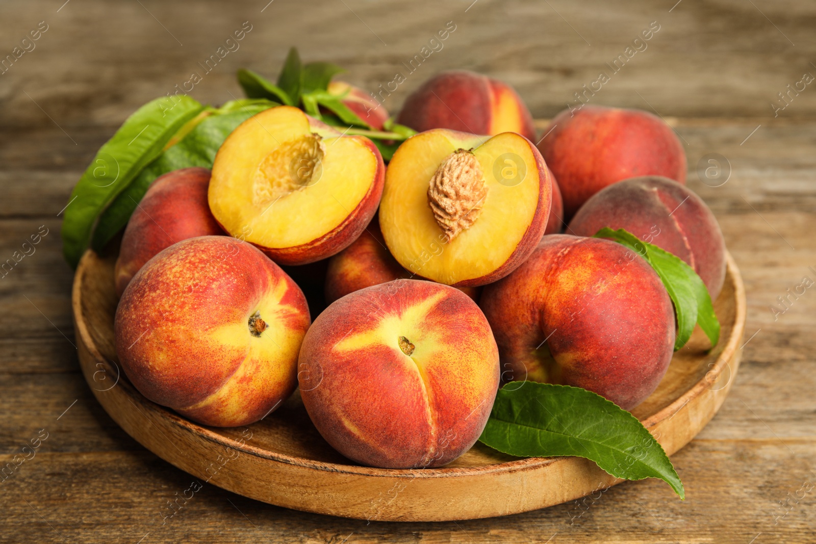 Photo of Plate with tasty fresh peaches and leaves on wooden table