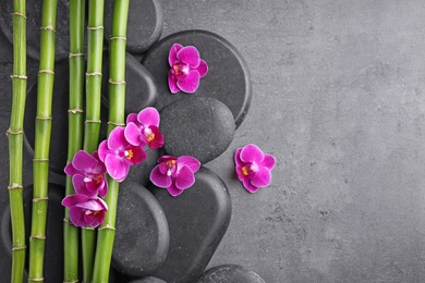 Flat lay composition with spa stones, bamboo and orchid flowers on grey background. Space for text