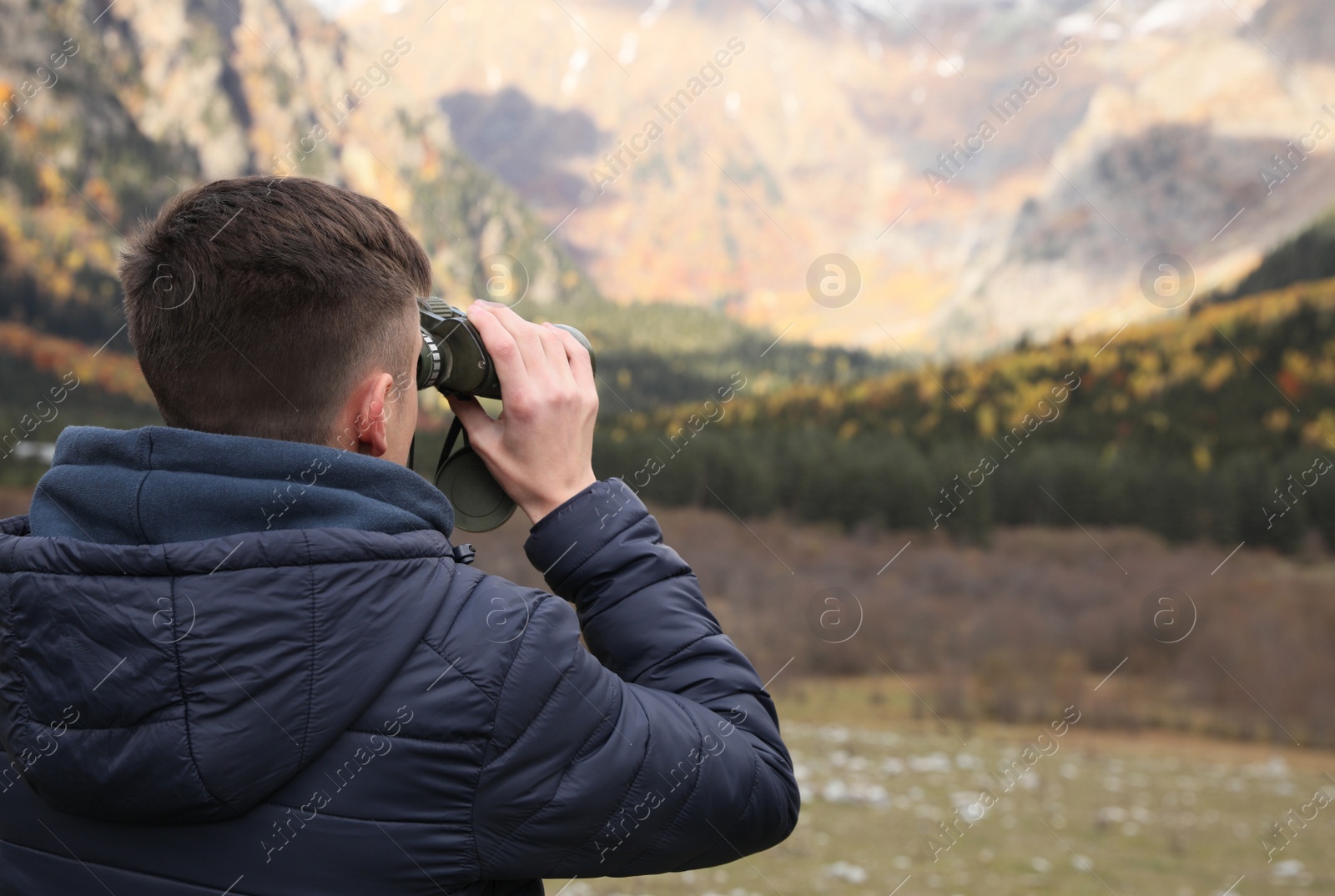 Photo of Boy looking through binoculars in beautiful mountains, back view. Space for text