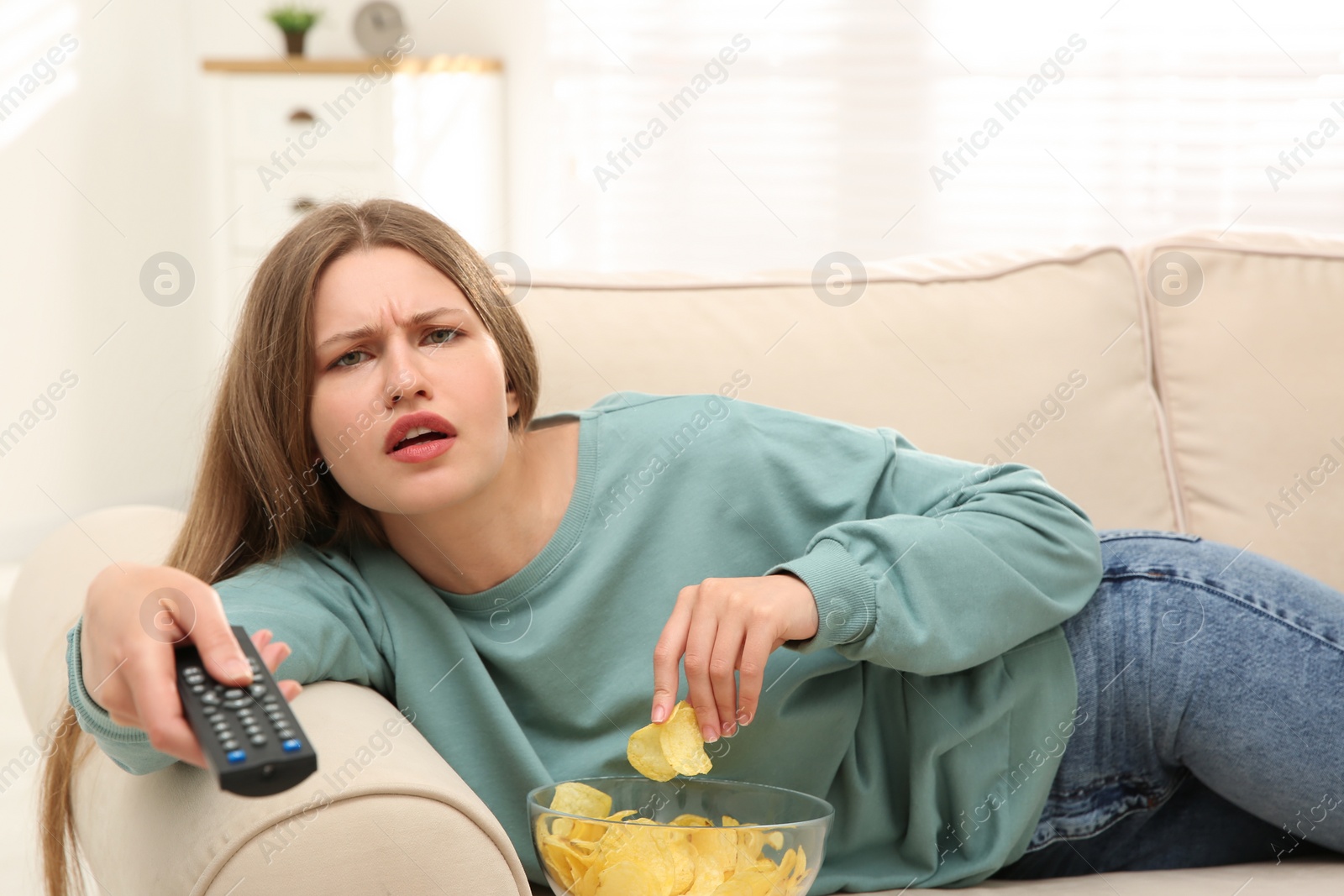 Photo of Lazy young woman with bowl of chips watching TV on sofa at home