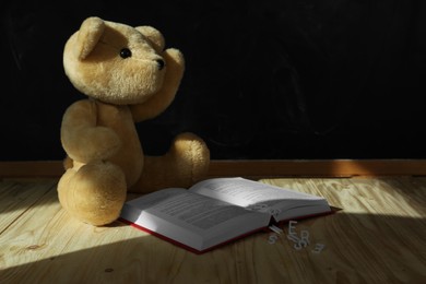 Photo of Dyslexia. Teddy bear with open book and letters on wooden table, space for text