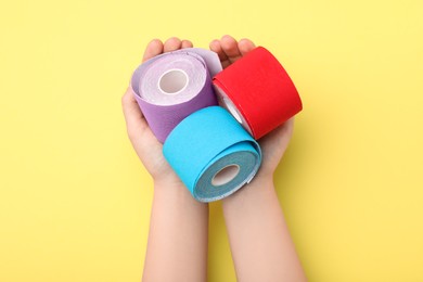 Photo of Woman with bright kinesio tape rolls at yellow table, top view
