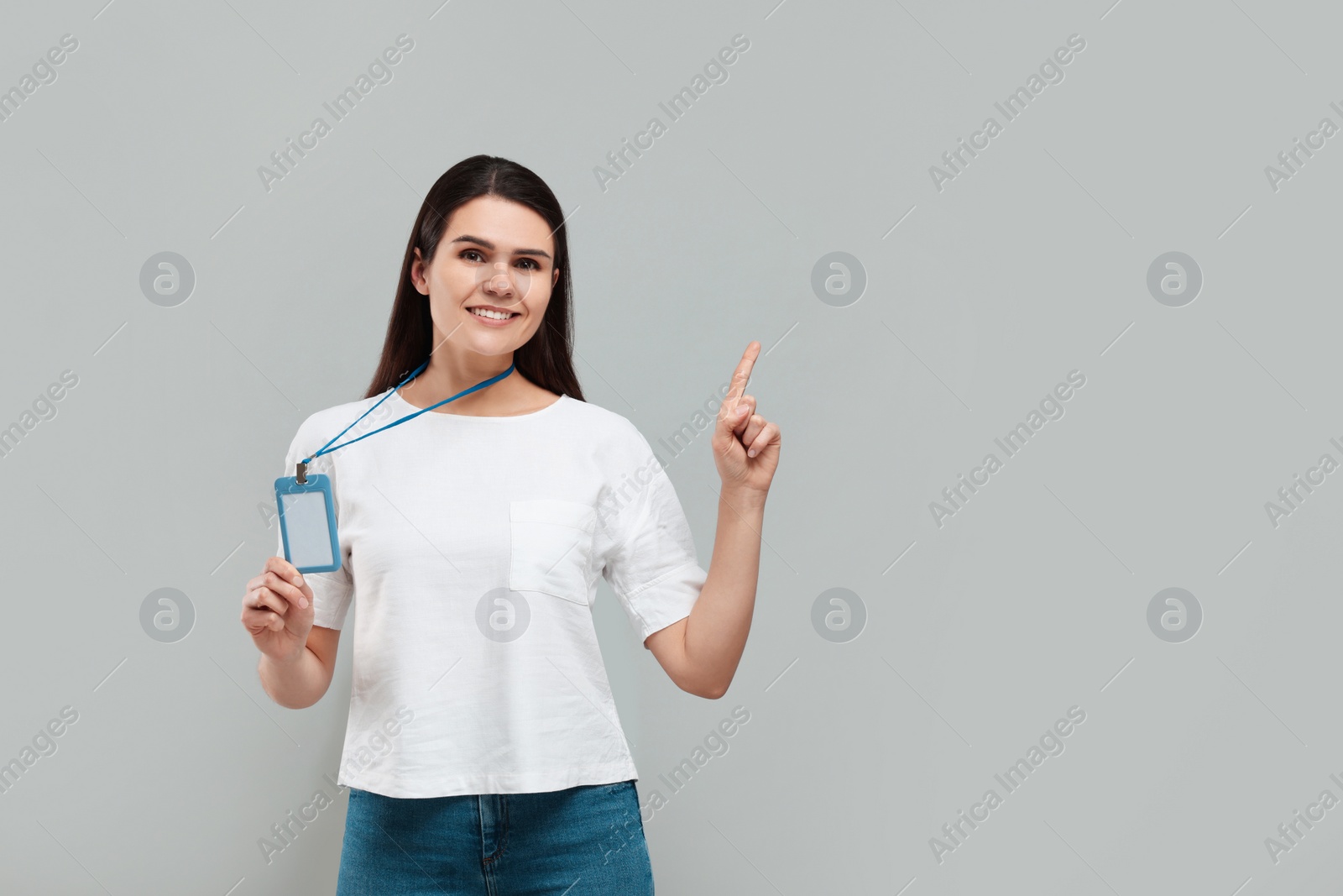 Photo of Smiling woman holding vip pass badge and pointing at something on grey background. Space for text