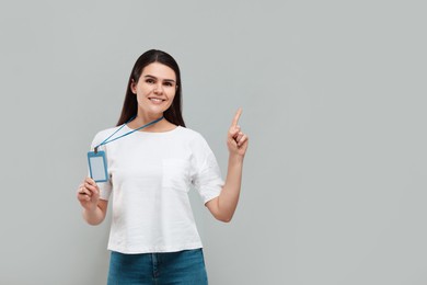 Smiling woman holding vip pass badge and pointing at something on grey background. Space for text