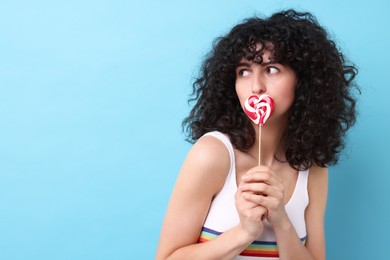 Beautiful woman with lollipop on light blue background, space for text