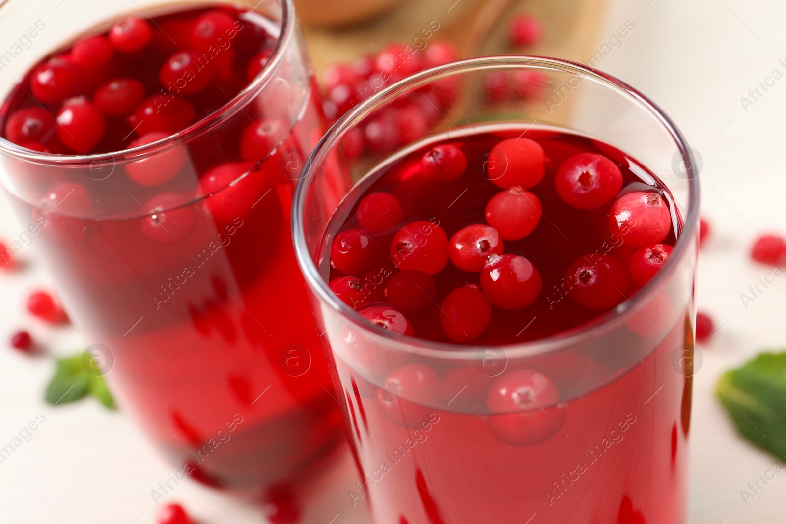 Photo of Tasty cranberry juice in glasses and fresh berries on white wooden table, closeup